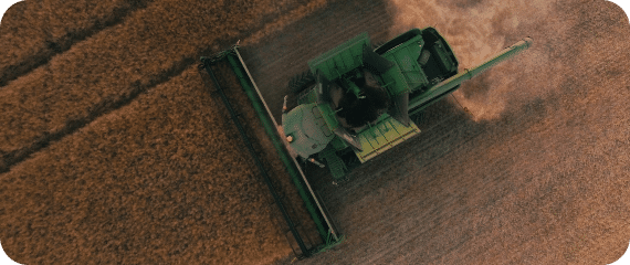 A green combine harvester cuts through a brown wheat field, leaving a trail of harvested crop.