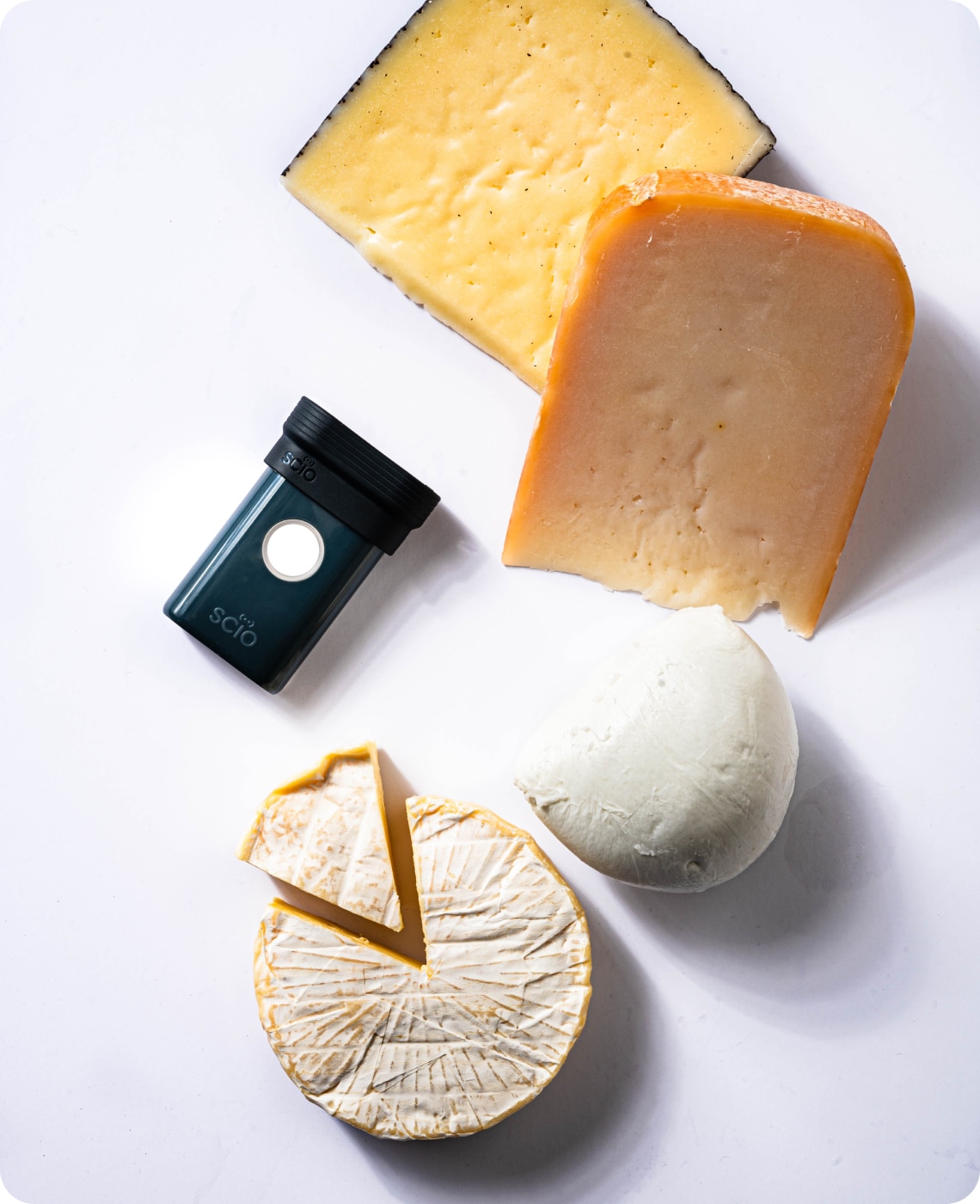 Various cheeses and a small black device with a white button are placed on a white surface.
