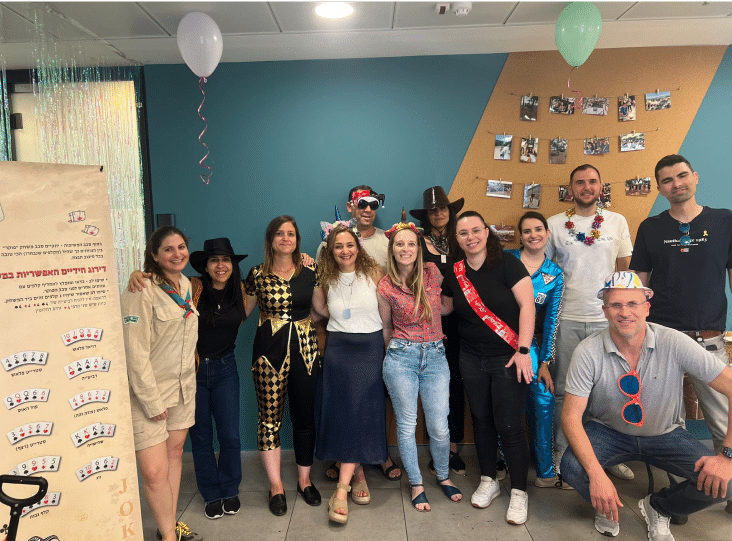 A group of people in costume poses inside a room decorated with balloons and photos on the wall.