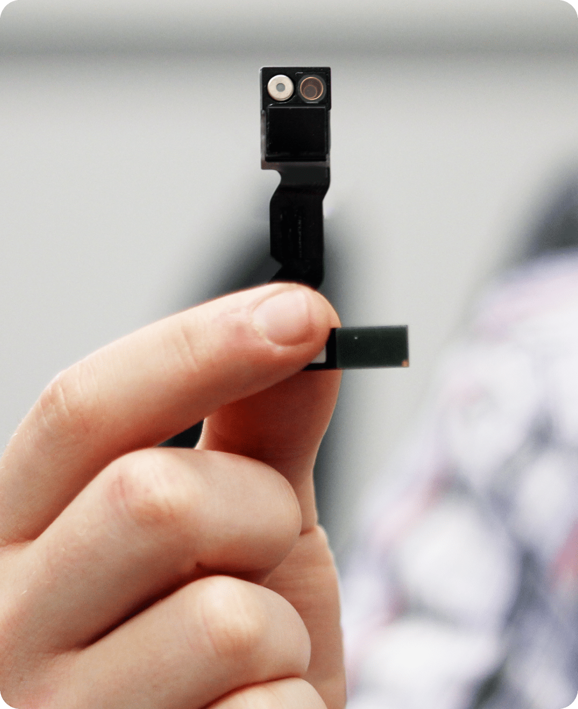 A hand holds a small electronic component with a camera module, featuring a lens and a tiny circuit board.